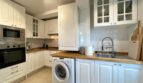 Moderne weiße Küche mit Holzarbeitsplatte, Einbaugeräten und Waschmaschine in Mallorca-Wohnung