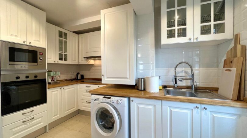 Moderne weiße Küche mit Holzarbeitsplatte, Einbaugeräten und Waschmaschine in Mallorca-Wohnung