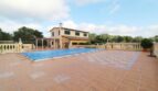 Finca Palma de Mallorca: Großer Pool mit blauer Abdeckung, Natursteintetrasse und mediterranem Herrenhaus im Hintergrund.