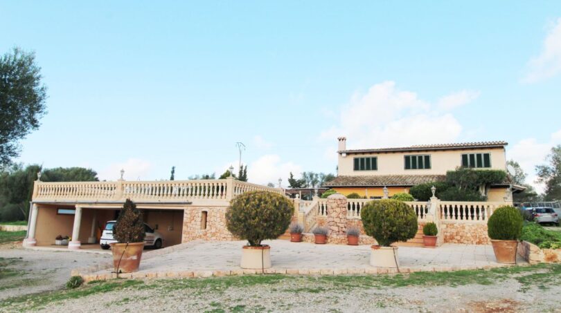 Außenansicht einer mediterranen Finca in Palma de Mallorca mit Steinmauer, Balustrade, Carport und gepflegten Buchsbäumen.