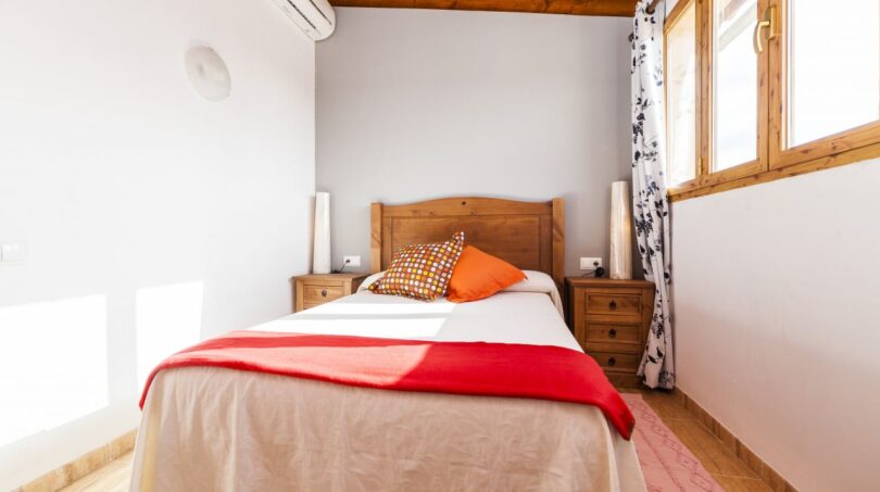 Schlafzimmer der Finca Palma de Mallorca mit Holzbett, roter Tagesdecke, Klimaanlage und Holzdecke