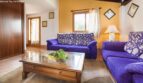 Helles Wohnzimmer der Finca mit lila Sofas, Holzcouchtisch und warmen Orangetönen an den Wänden.
