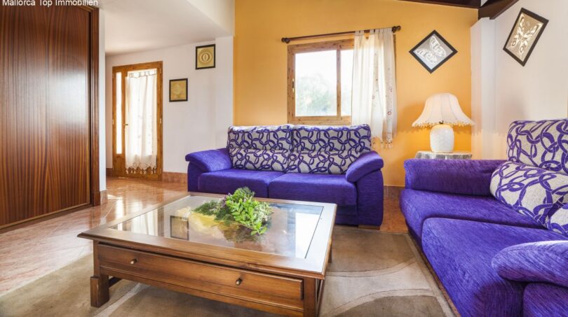 Helles Wohnzimmer der Finca mit lila Sofas, Holzcouchtisch und warmen Orangetönen an den Wänden.