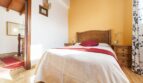 Schlafzimmer der Finca mit Doppelbett, Holzmöbeln, gelber Akzentwand und Terrakottaboden in Palma de Mallorca