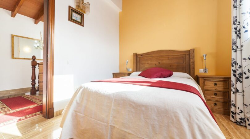 Schlafzimmer der Finca mit Doppelbett, Holzmöbeln, gelber Akzentwand und Terrakottaboden in Palma de Mallorca