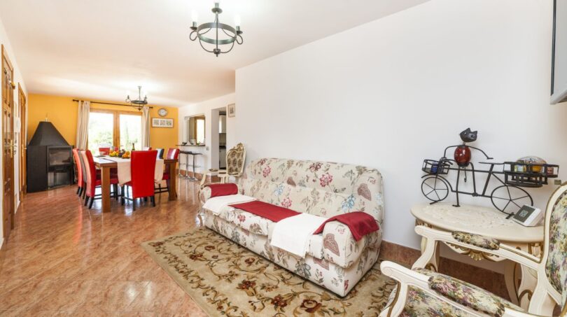Wohnzimmer der Finca mit Blumensofa, Esstisch, roten Stühlen und Kamin in Palma de Mallorca