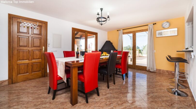 Helles Esszimmer der Finca mit großem Holztisch, roten Lederstühlen und Kamin für bis zu 10 Gäste.