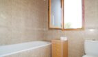 Badezimmer der Finca mit Badewanne, Holzfenster, beigen Fliesen und kleinem Rollcontainer