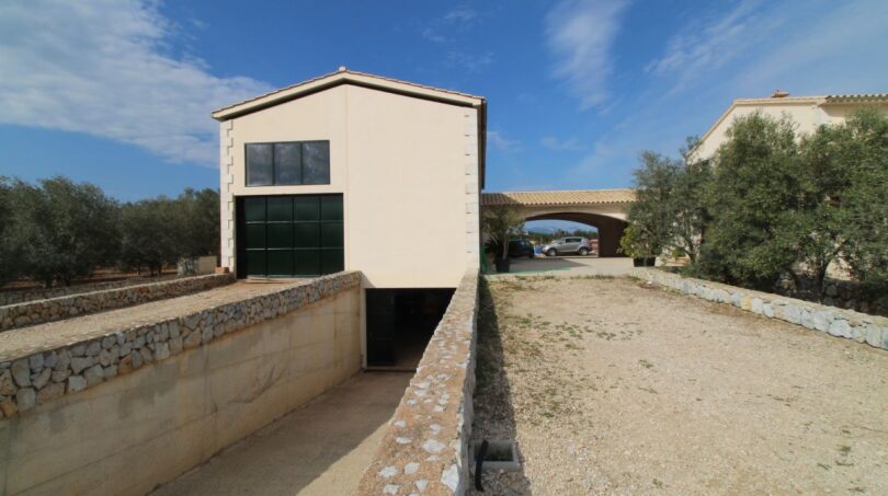 Neubau-Finca Son Liebre: Modernes Nebengebäude mit Garage, Natursteinmauern und Zufahrt zur Hauptfinca.