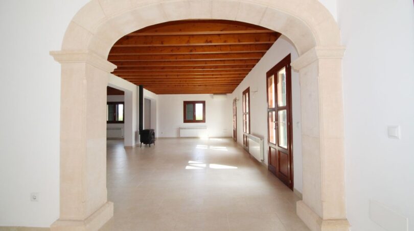 Geräumiger Wohnbereich mit Natursteinbogen, Holzbalkendecke und Terrakottafliesen in Neubau-Finca Palma