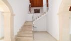 Heller Eingangsbereich der Neubau-Finca mit Marmortreppe, Steinbögen und Holzbalkendecke im Obergeschoss.