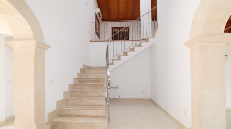 Heller Eingangsbereich der Neubau-Finca mit Marmortreppe, Steinbögen und Holzbalkendecke im Obergeschoss.