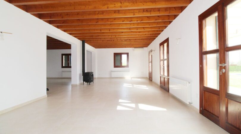 Geräumiges Wohnzimmer der Neubau-Finca mit Holzbalkendecke, Kaminofen und Terrassentür in Son Liebre.