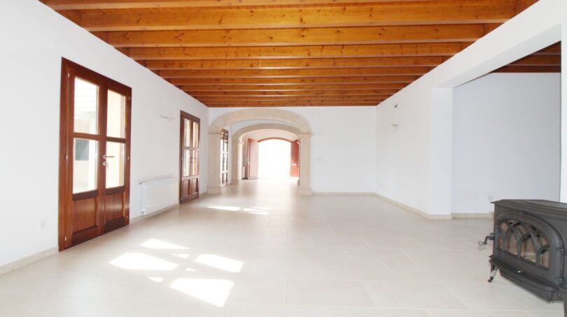 Geräumiges Wohnzimmer der Neubau-Finca mit Holzbalkendecke, Steinbogen und Kaminofen in Son Liebre