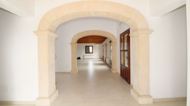 Weitläufiger Eingangsbereich mit elegantem Steinbogen, Holzdecke und weißen Wänden in Neubau-Finca, Palma