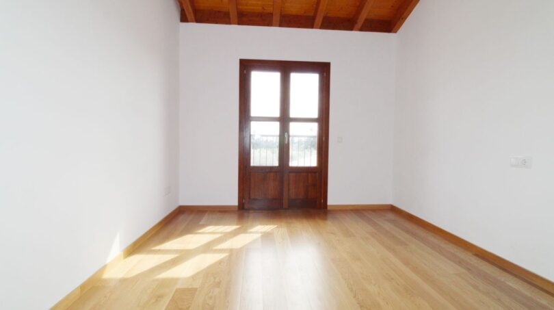 Helles, leeres Zimmer mit Holzdielen, Holzbalkendecke und Terrassentür in Neubau-Finca, Palma