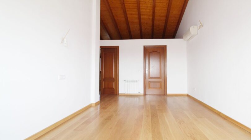 Helles leeres Zimmer mit Holzbalkendecke, Parkettboden und zwei Holztüren in Neubau-Finca Palma