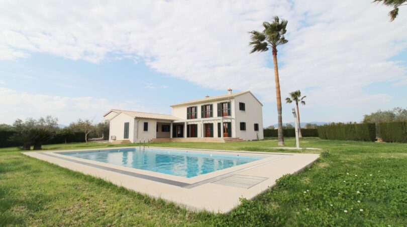 Außenansicht Neubau-Finca Son Liebre: weißes Landhaus mit Pool, Palmen und gepflegtem Rasen.