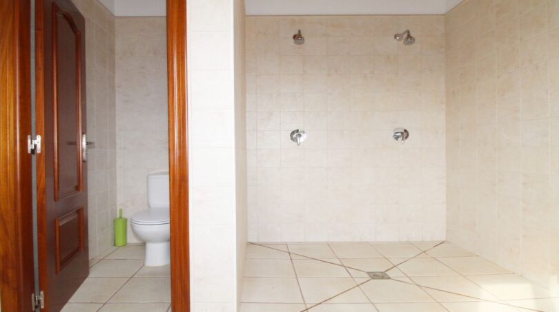Geräumiges Badezimmer der Finca mit Doppeldusche, weißen Fliesen und separatem WC-Bereich mit Holztür.
