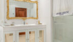 Elegantes Badezimmer der Luxusvilla mit goldenem Barockسpiegel, weißem Waschtisch und Glasdusche.