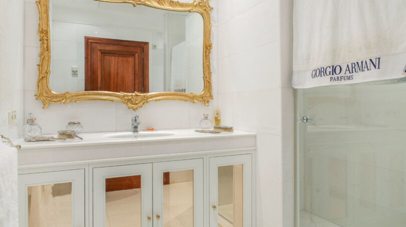 Elegantes Badezimmer der Luxusvilla mit goldenem Barockسpiegel, weißem Waschtisch und Glasdusche.