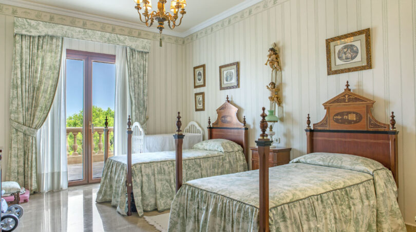 Elegantes Schlafzimmer der Luxusvilla in Llucmajor mit zwei Einzelbetten, Kronleuchter und Balkon mit Meerblick.