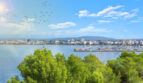 Vista panorámica de la costa de Llucmajor con puerto deportivo, mar turquesa y silueta de la ciudad ante montañas.