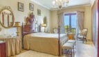 Elegantes Schlafzimmer der Luxusvilla mit antikem Himmelbett, Kronleuchter und Meerblick durch Terrassentür.