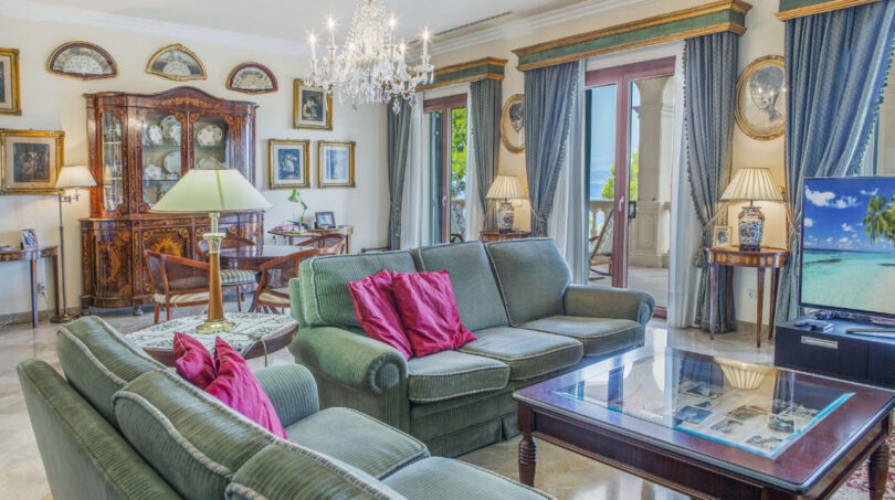 Elegantes Wohnzimmer der Luxusvilla in Llucmajor mit Kronleuchter, grünen Sofas und Meerblick.