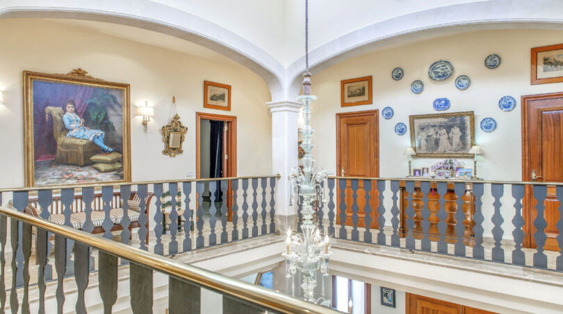 Eleganter Galerieflur der Luxusvilla in Llucmajor mit Kronleuchter, Gemälden und blau-weißem Balustergeländer.