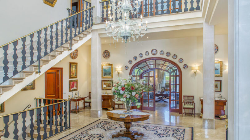 Repräsentative Einganghalle der Luxusvilla mit Kristallkronleuchter, Marmorboden und elegantem Treppenaufgang.