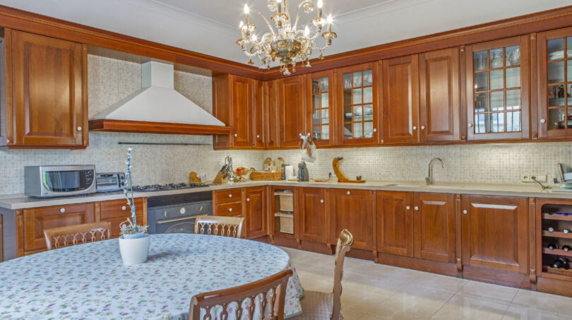 Geräumige Küche der Luxusvilla in Llucmajor mit Holzschränken, Esstisch und elegantem Kronleuchter.