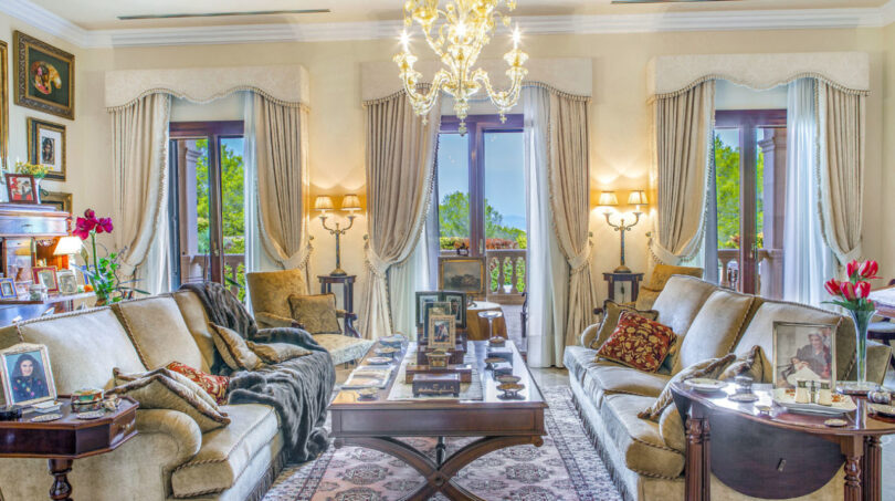 Elegante sala de estar de la villa de lujo en Llucmajor con lámpara de araña, sofás de terciopelo y vista al mar a través de altas puertas de terraza.