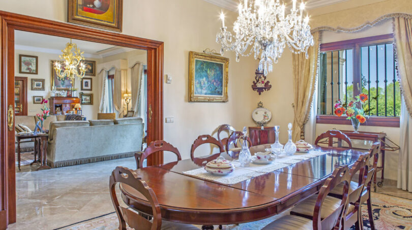 Elegantes Esszimmer der Luxusvilla in Llucmajor mit Kristallleuchter, antikem Holztisch und Blick ins Wohnzimmer.