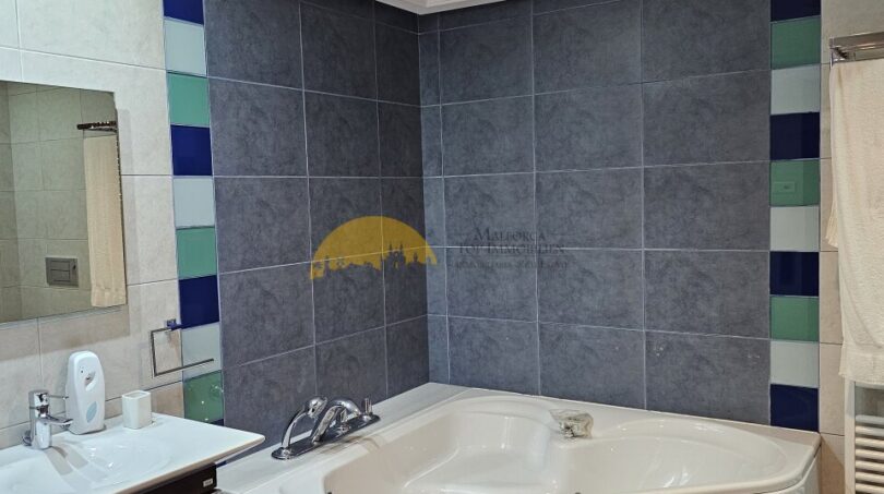 Badezimmer des Stadthauses in Inca mit Eckbadewanne, grauen Fliesen und bunten Akzenten