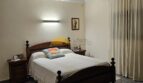 Schlafzimmer mit Doppelbett aus Holz, Nachttischen, Wandlampe und hellen Vorhängen im Stadthaus Inca