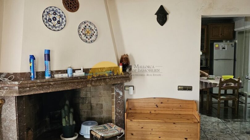 Wohnzimmer der Finca bei Inca mit Marmorkamin, Holzbank und dekorativen Keramiktellern an der Wand.