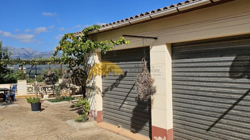 Doppelgarage der Finca bei Inca mit Rolltor, Weinranke und Bergblick unter blauem Himmel.
