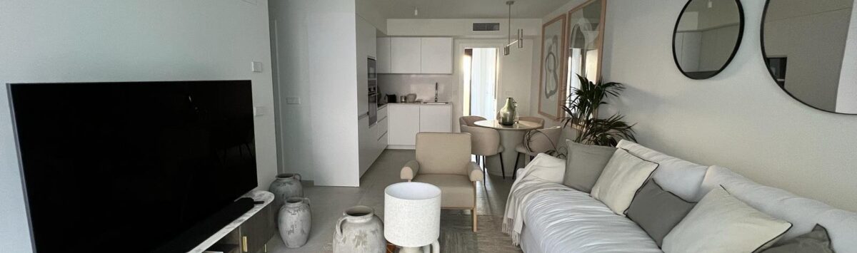 Helles Wohnzimmer mit weißem Sofa, modernem TV und offener Küche in exklusiver Wohnung in Palma
