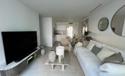 Helles Wohnzimmer mit weißem Sofa, modernem TV und offener Küche in exklusiver Wohnung in Palma