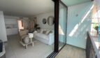 Balkon mit Blick in hellen Wohnraum, weiße Couch, runde Spiegel, offene Küche – modernes Apartment in Palma de Mallorca