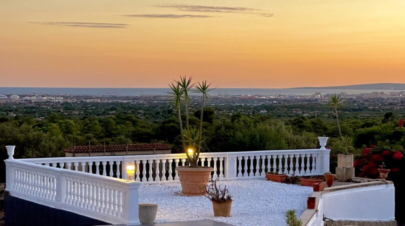 Weitläufige Dachterrasse mit weißem Baluster, Palmen und Panoramablick über Marratxí bis zum Meer bei Sonnenuntergang.