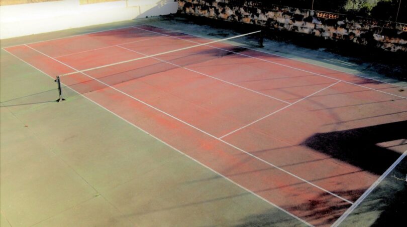 Roter Tennisplatz mit Netz, Steinmauer und Bäumen der Luxusvilla in Marratxí