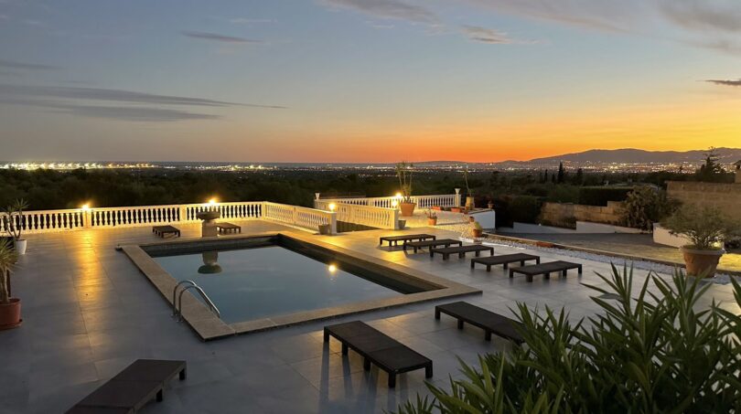 Beleuchteter Pool mit Panoramablick auf Marratxí bei Sonnenuntergang, umgeben von eleganten Liegestühlen.