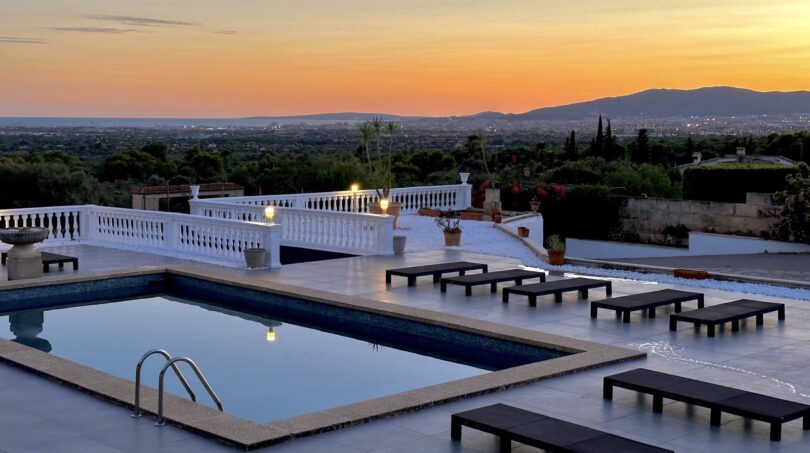 Infinity-Pool mit Sonnenliegen bei Sonnenuntergang, Blick über Marratxí bis zu den Bergen.