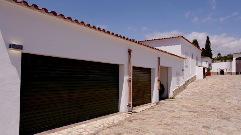 Weiße Finca-Fassade mit Terrakotta-Dach, zwei Garagentoren und gepflastertem Innenhof in Marratxí.