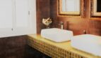 Elegantes Doppelwaschtisch-Bad mit Goldmosaik-Ablagefläche, dunklen Fliesen und ornamentalen Spiegeln in Marratxí-Villa