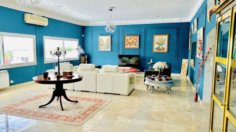 Elegantes Wohnzimmer mit blauem Wanddesign, Marmorboden, weißer Couch und Gemälden in Marratxí-Villa.