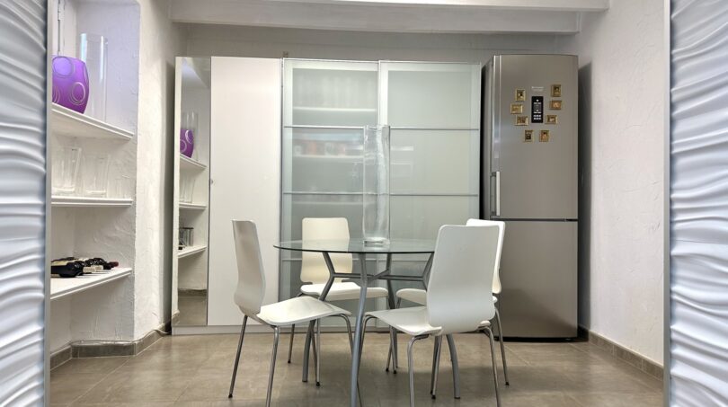 Helles Esszimmer mit Glasstisch, weißen Stühlen, Einbauschrank und Kühlschrank in modernem Ambiente in Marratxí.