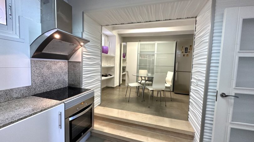 Moderne Küche mit Granit-Arbeitsfläche und Blick in eleganten Essbereich mit Glasfalttür in Marratxí.